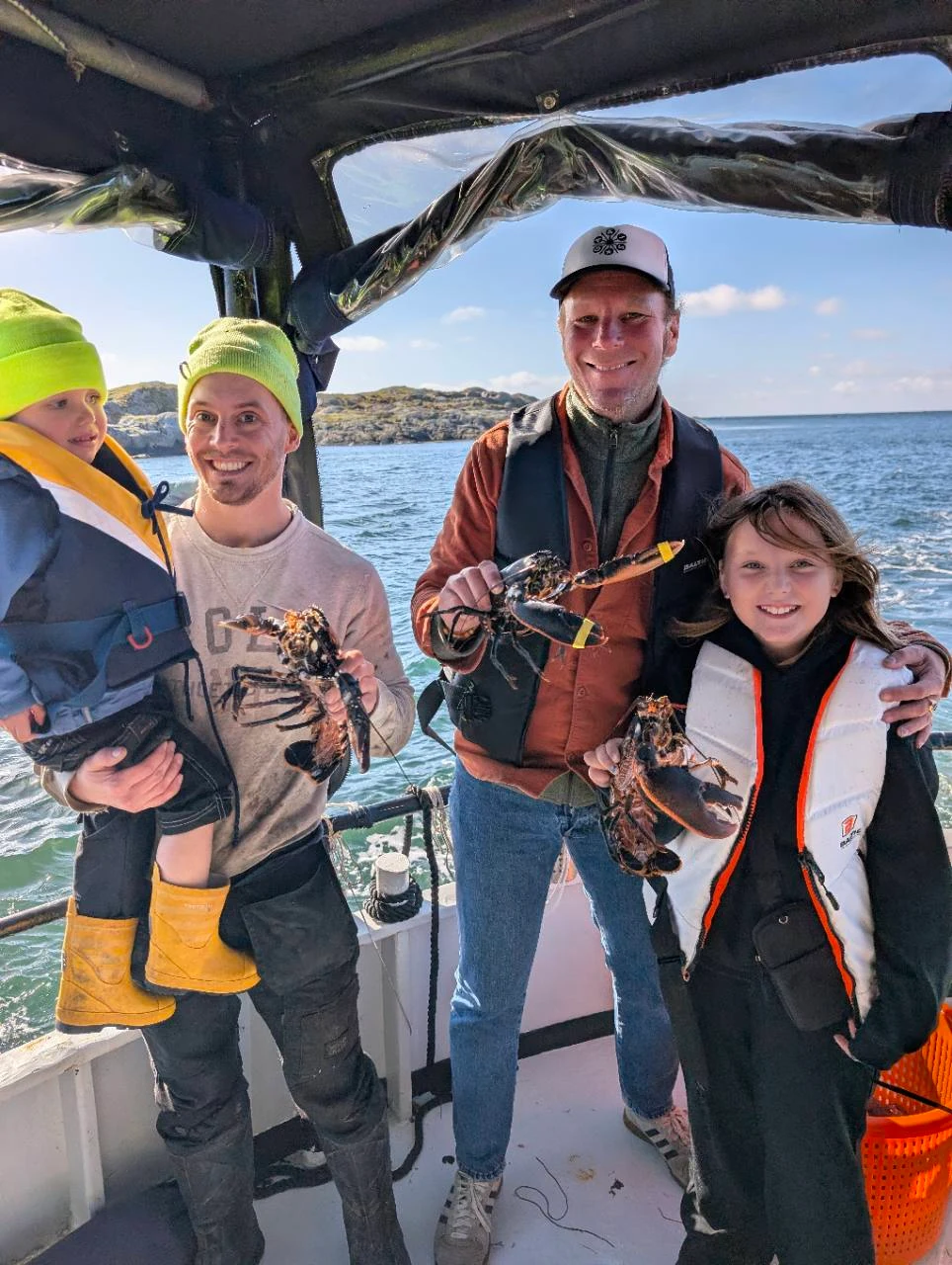 Fyra personer ombord på en båt, med humrar och havet i bakgrunden.