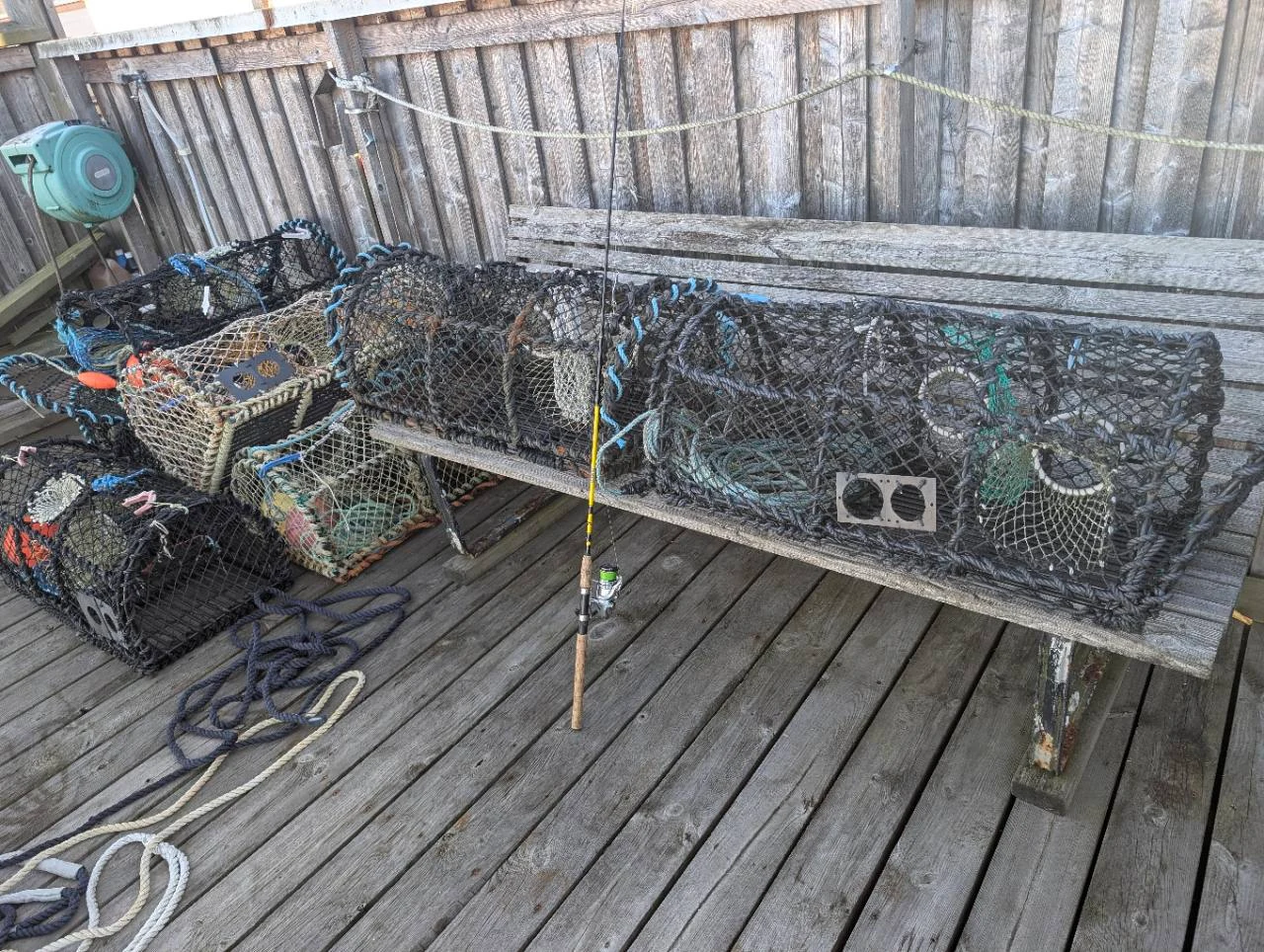 Hummertinor, rep och ett fiskespö på trädäcket vid varvet.