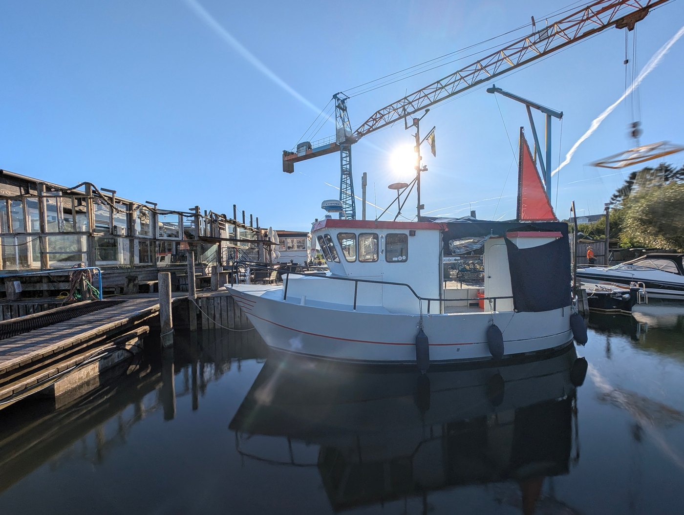 En vit båt vid bryggan under varvets kran på Brännö.